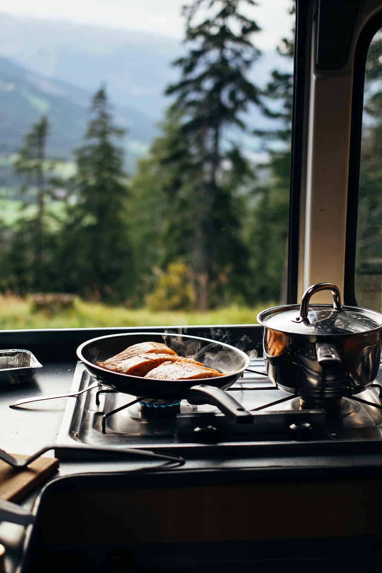 Close up on frying pan with organic salmon prepared in inside camper van on campsite in mountains or forest. Life on the road, camper van lifestyle outdoors vibes. Prepare food in converted vehicle